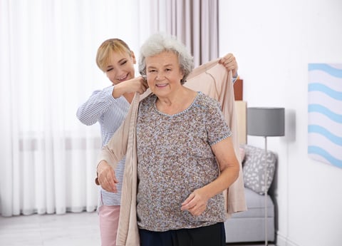 Female nurse assisting an older woman patient put on a sweater