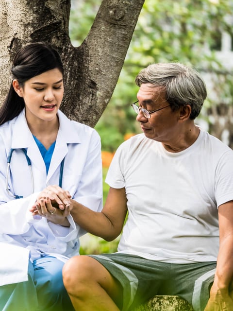 Female doctor holding the hand of an older male patient