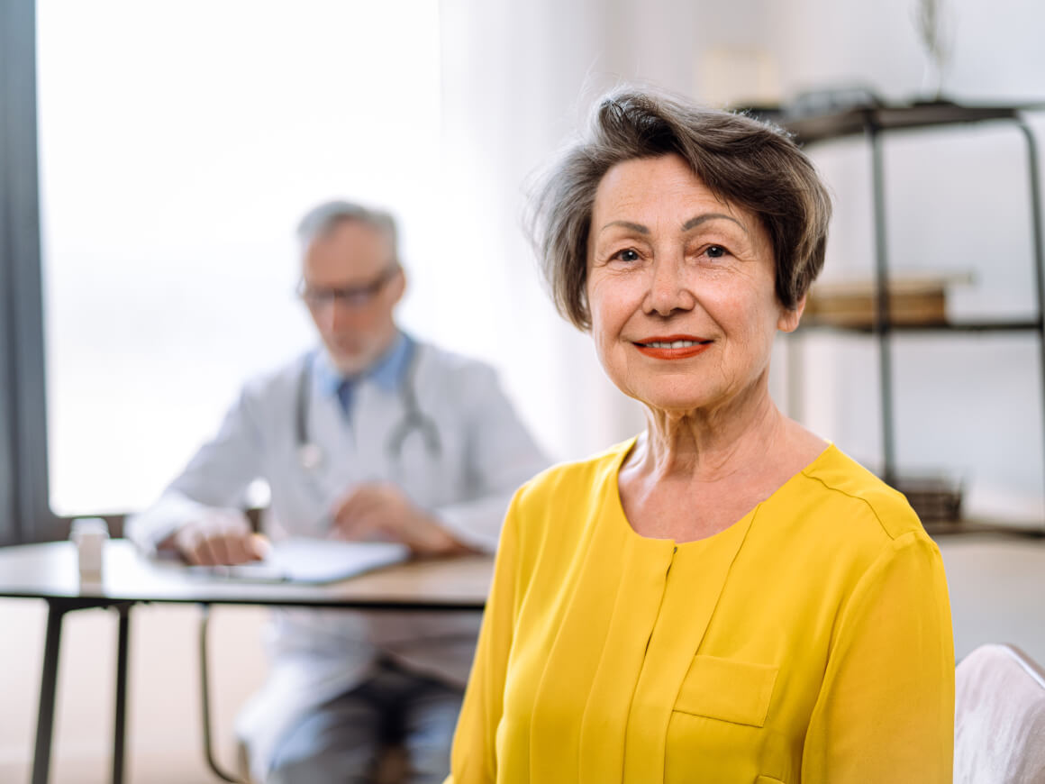 Older woman sitting in an office with a blurred out doctor in the background